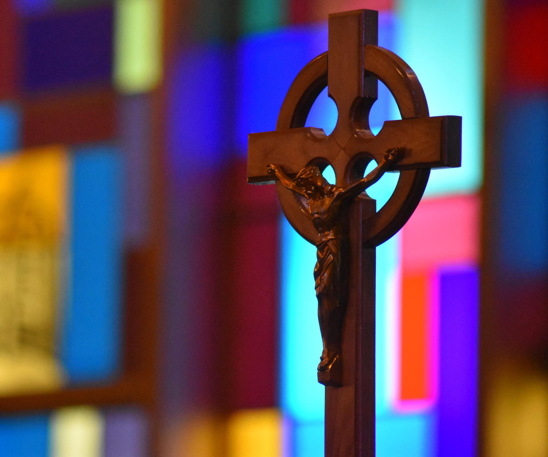 A wooden crucifix at Holy Cross Lutheran Church in Racine, Wisconsin, set in front of the out-of-focus stained glass windows.